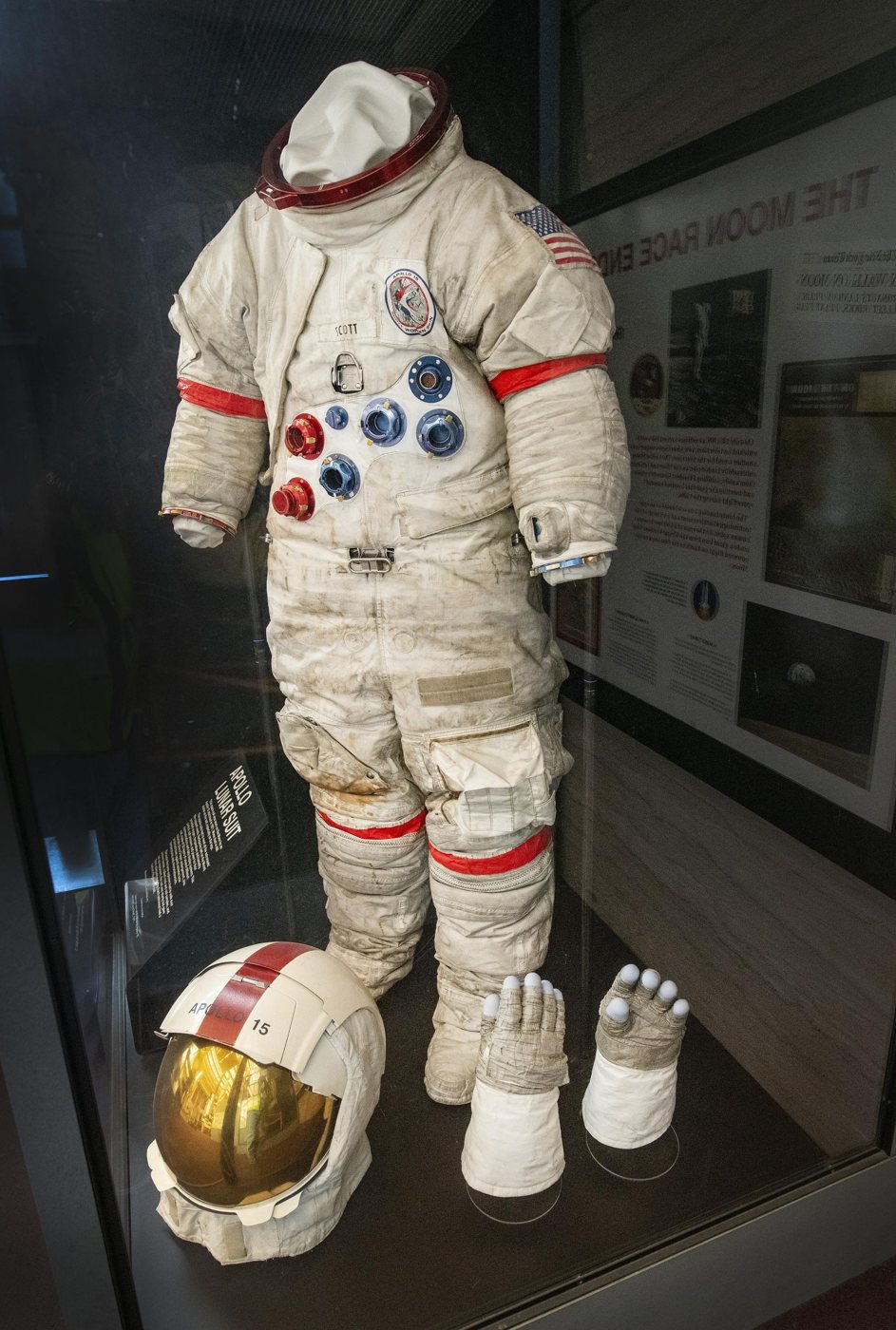 The same suit in a display case in 2021, helmet and gloves beside it